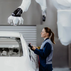 Mitarbeitende Person steuert einen Lackierroboter an einer Fahrzeugkarosserie.