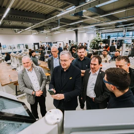 Group of people in a modern training center surrounded by workbenches and technical equipment, with others engaged in conversations in the background