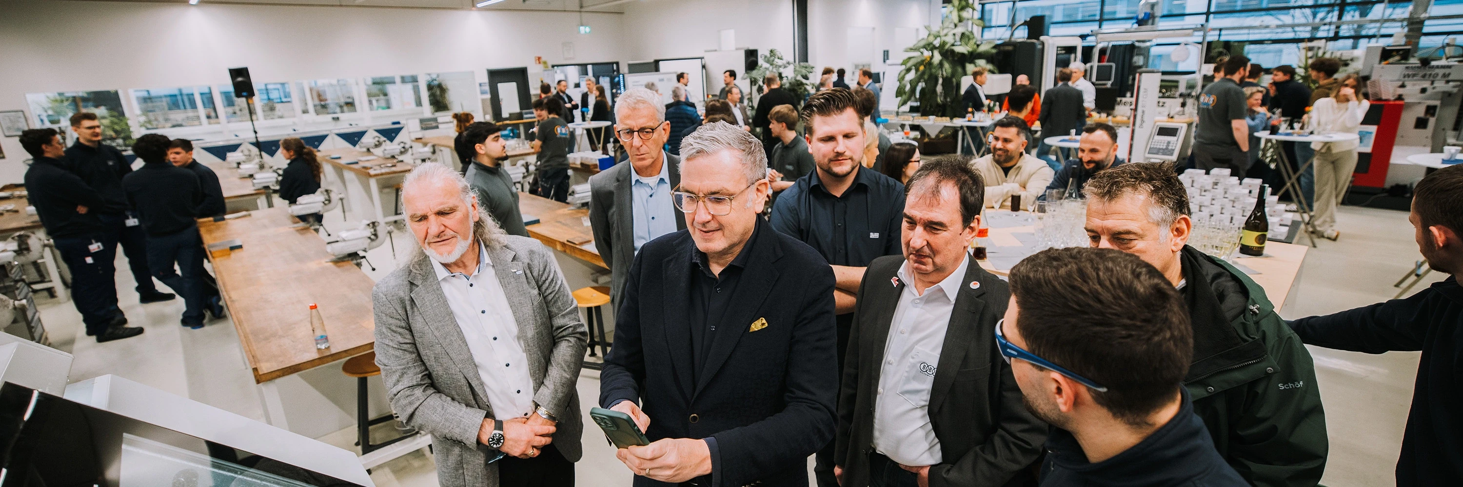 Group of people in a modern training center surrounded by workbenches and technical equipment, with others engaged in conversations in the background