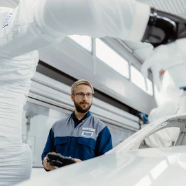 Innovation hub Worker monitoring the painting process on a vehicle body with a robot arm.