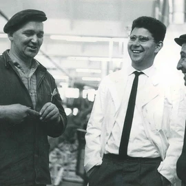 Heinz Dürr lachend im Gespräch mit zwei Angestellten